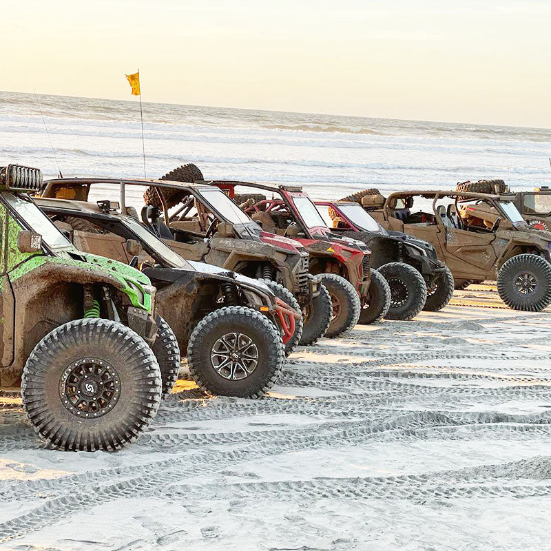DIRT WARRIOR ACCESSORIES UTV / SXS windshields, vault enclosures, windshield wipers, accessories - DWA Row of UTV / SXS off-road vehicles on a sandy surface with a clear sky.