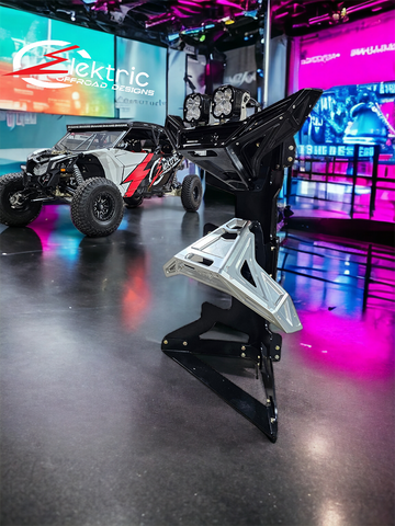 A black metal bumper display stand with red accents, designed for showcasing vehicle bumpers, displayed in a showroom setting with a offroad vehicle in the background. Elektric Offroad Designs Bumper Display Stand